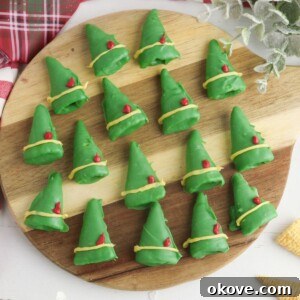 A vibrant display of chocolate coated green Bugle chips, creatively decorated to resemble elf hats with cheerful yellow bands and tiny red feathers, presented on a rustic round wooden cutting board.