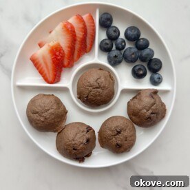 Five chocolate veggie muffins on a white divided plate with fresh strawberries and blueberries, ready for a healthy snack.