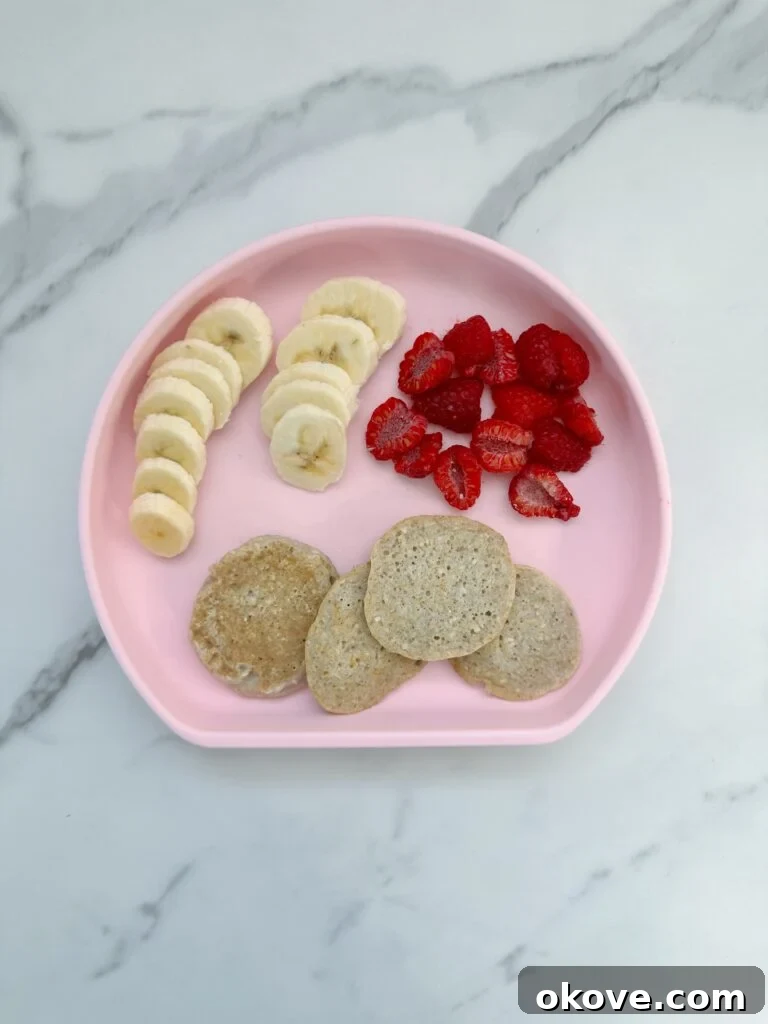 Simple Eggless Pancake Perfection 2 Several 3 ingredient egg free pancakes on a pink plate with sliced raspberries and bananas, ready to be served to toddlers or babies.
