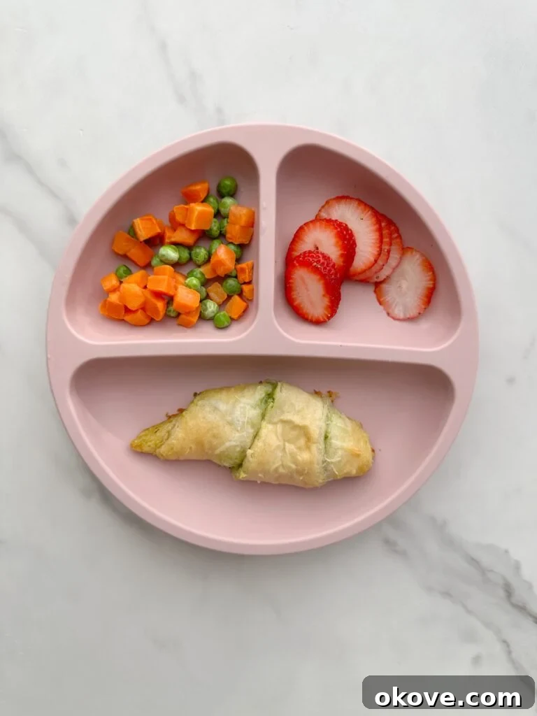 A divided plate with a spinach pesto mozzarella roll-up and sliced strawberries, showcasing a delicious and healthy meal for kids.