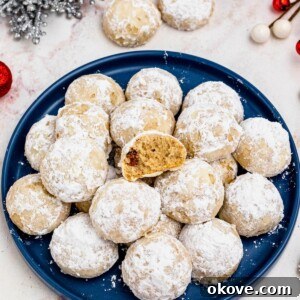 Powdered Cloud Kisses 11 Powder sugar coated Snowball cookies, stacked on a blue plate with holiday party favors on the table around the plate, with one cookie missing a bite.