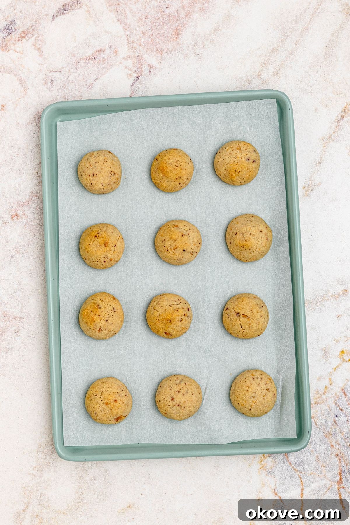 Powdered Cloud Kisses 7 Golden brown baked snowball cookies on a baking sheet, fresh out of the oven.