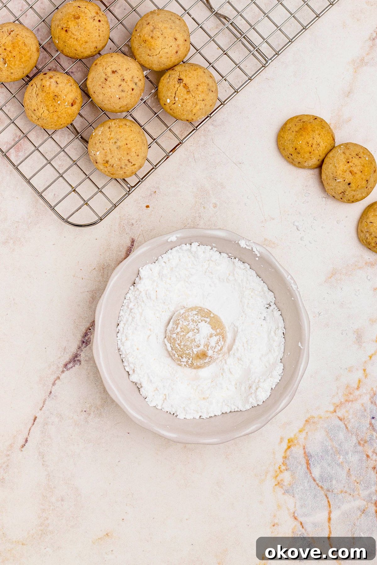 Powdered Cloud Kisses 9 Baked cookies being rolled in small shallow bowl of powered sugar for a snowy finish.