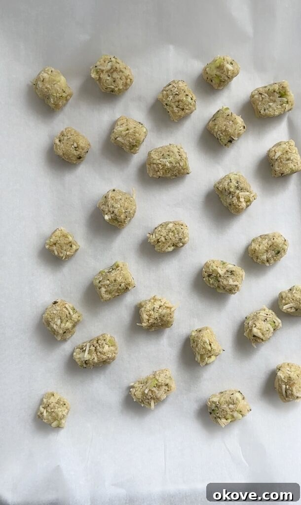 Crispy Parmesan Zucchini Bites 8 A baking sheet lined with parchment paper, filled with numerous perfectly baked and golden-brown zucchini parmesan tots, fresh out of the oven.