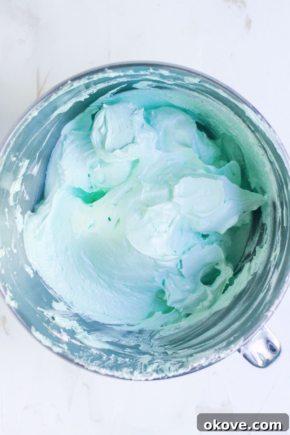 Green coloring and vanilla extract added to meringue in a silver bowl. 