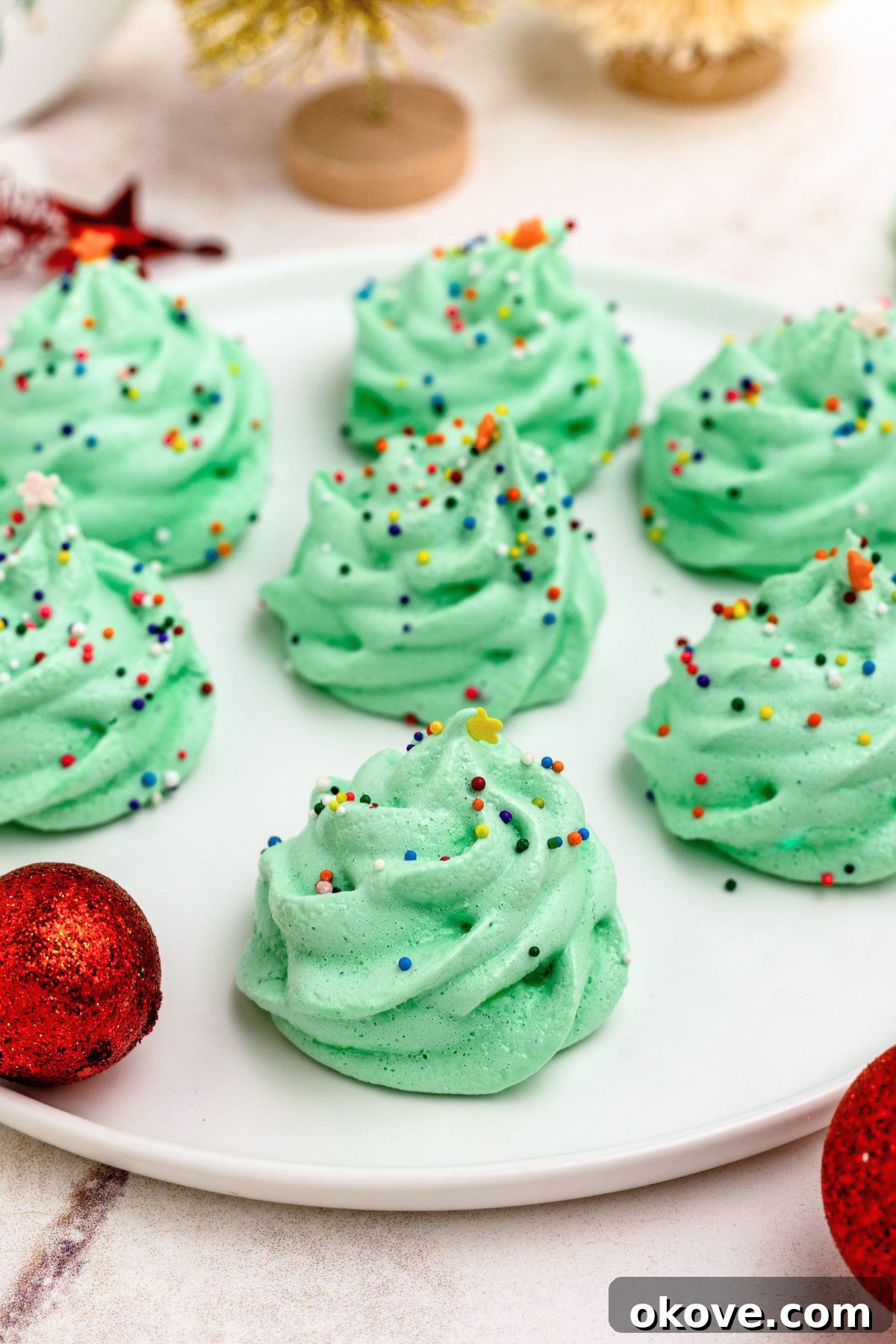 Green meringue trees on a white plate, with ornaments around the plate. 