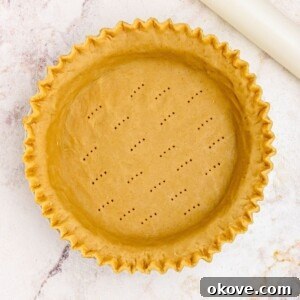 Golden uncooked pie crust in a pie plate, with fluted fork holes.