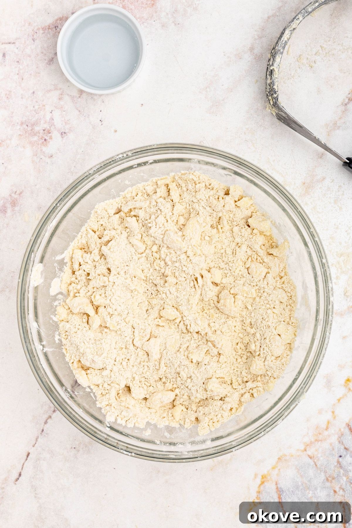 Butter, mixed with flour and other dry ingredients, in a clear glass bowl, before adding water, to make a homemade pie crust.