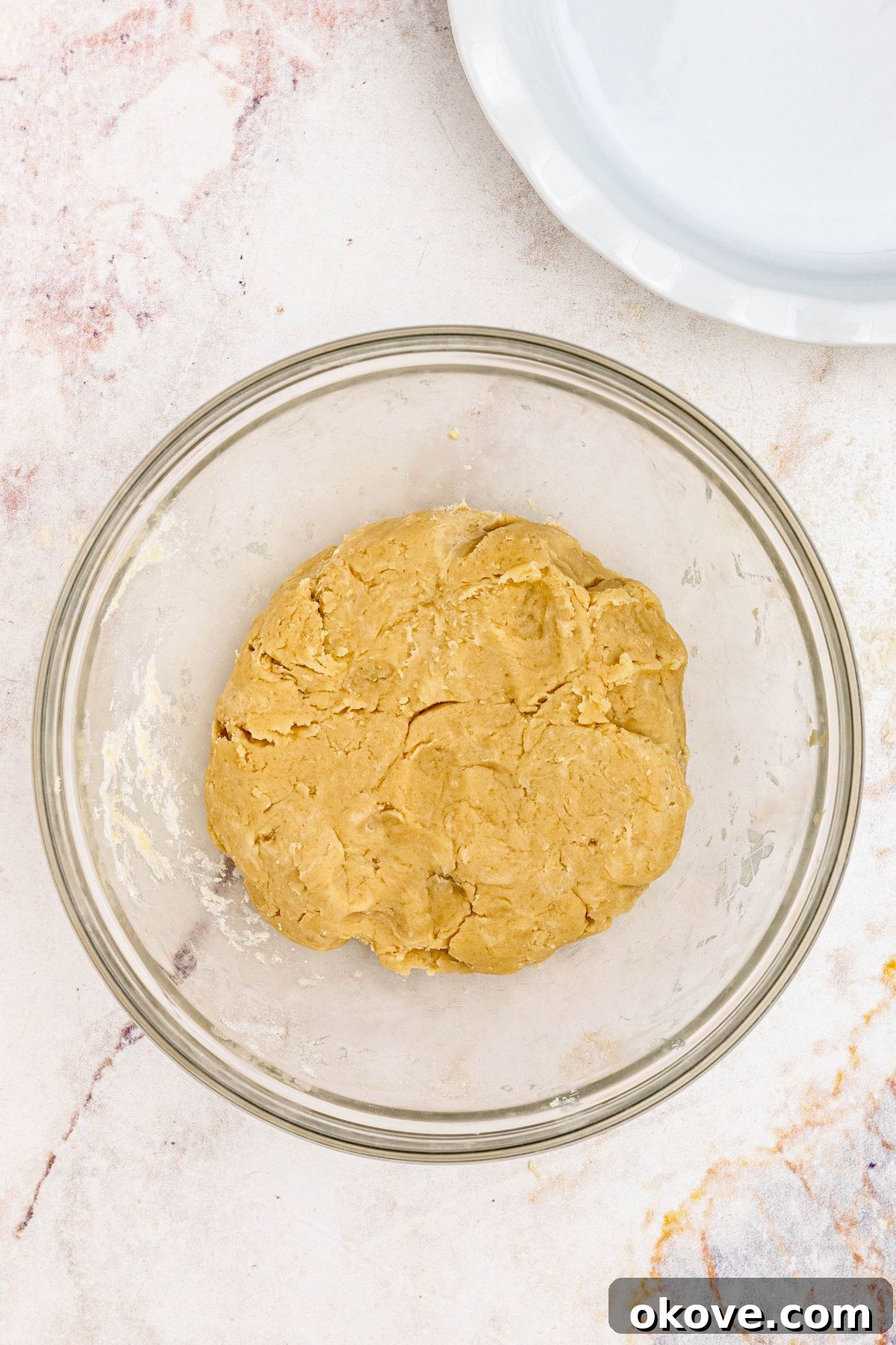 Ball of golden pie crust dough in a clear glass bowl.