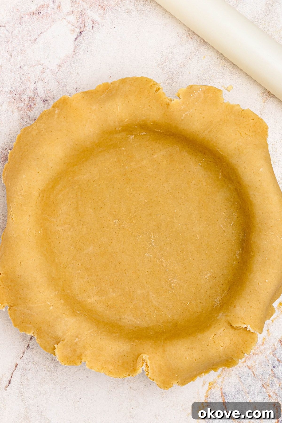 Golden pie crust rolled into pie plate, before trimming the edges.
