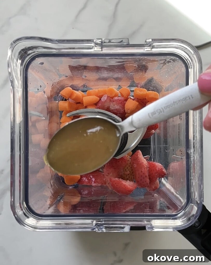 Fruit & Veggie Blend in Blender A blender filled with fresh strawberries, chopped carrots, honey, and water, ready to be blended into a smooth mixture.