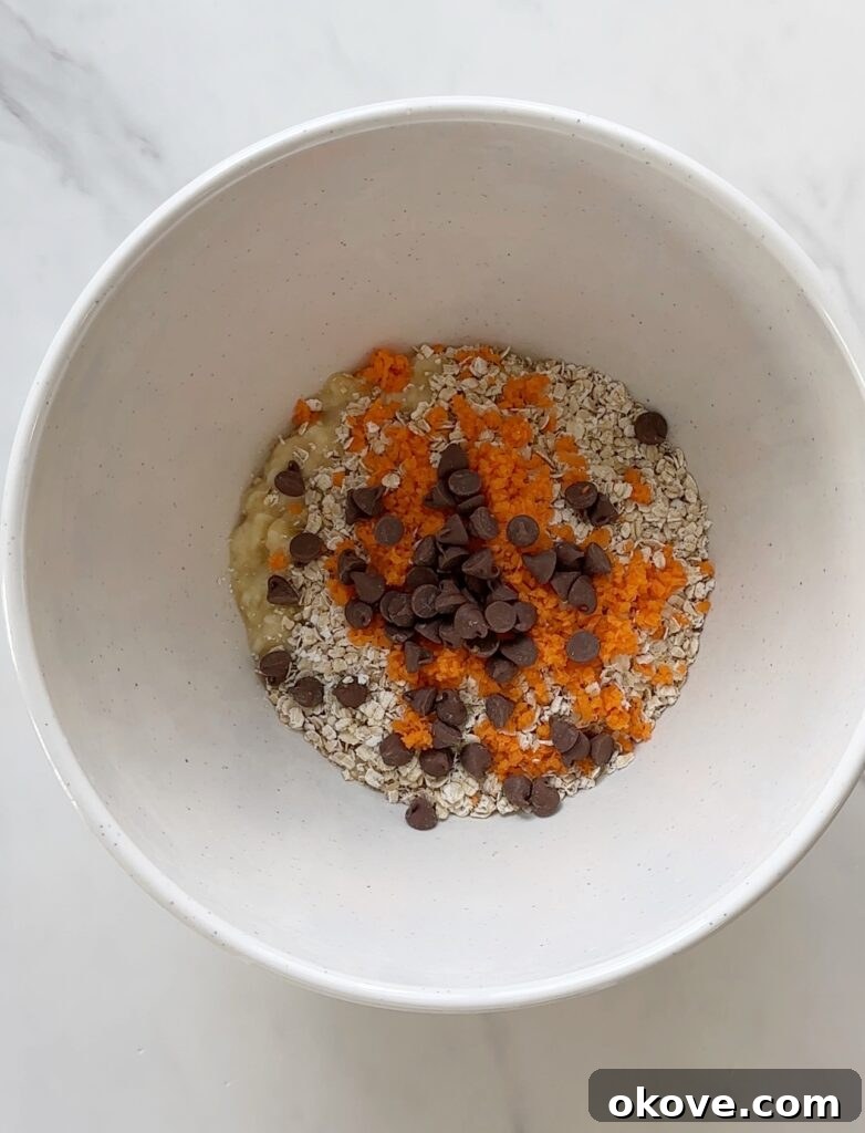 Golden Carrot Banana Oat Delights 6 Ingredients for banana carrot oat cookies, including mashed bananas, oats, and grated carrots in a bowl.