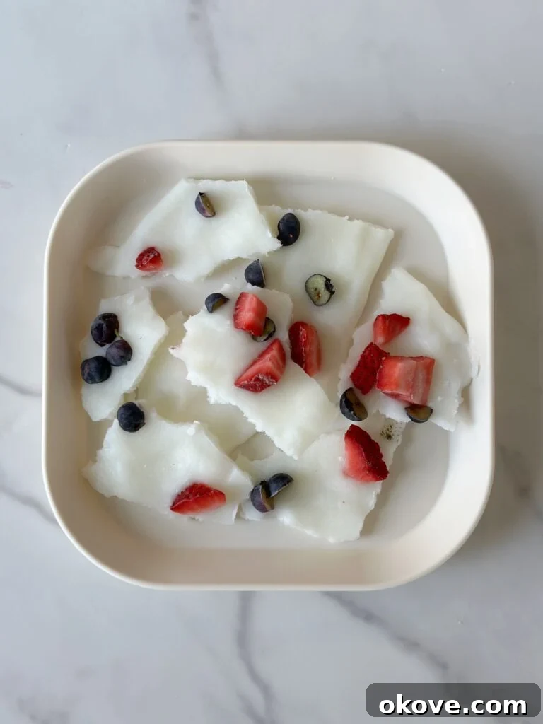 Delightful frozen yogurt bark pieces, artfully arranged on a white plate and garnished with fresh, vibrant strawberries and blueberries.