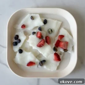 A close-up shot of frozen yogurt bark with strawberries and blueberries, ready to be enjoyed.