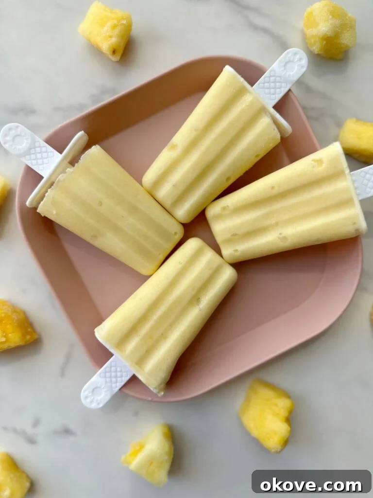 Dreamy Two-Ingredient Dole Whip Pops 2 Four dole whip popsicles on a pink plate with pineapple chunks around them