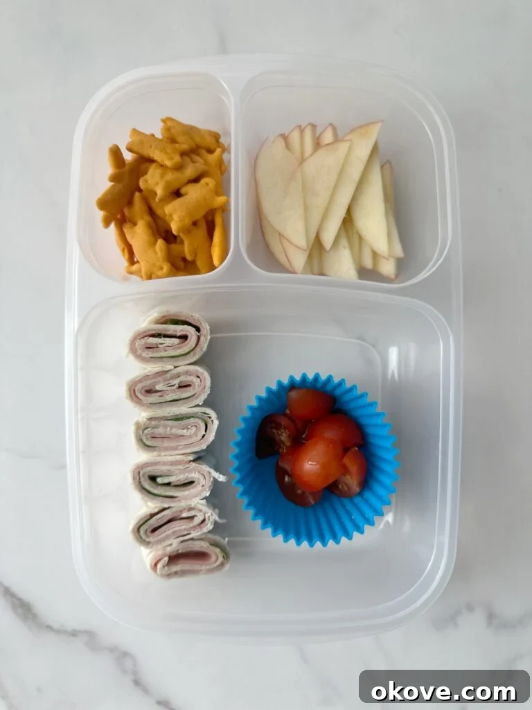 Lunchbox Magic for Toddlers 3 Several sandwich roll-ups, chopped tomatoes, apple slices, and cheese crackers in a plastic food storage container