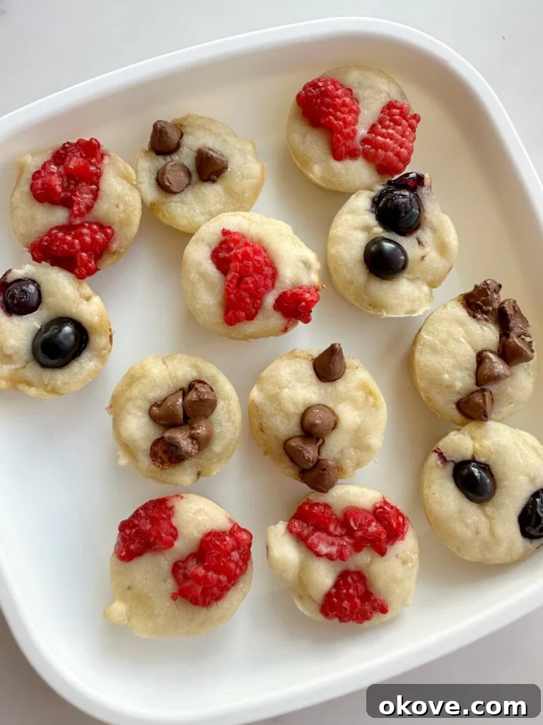 Grab-and-Go Pancake Bites 2 A white plate with several baked pancake bites that are topped with either raspberries blueberries or chocolate chips.
