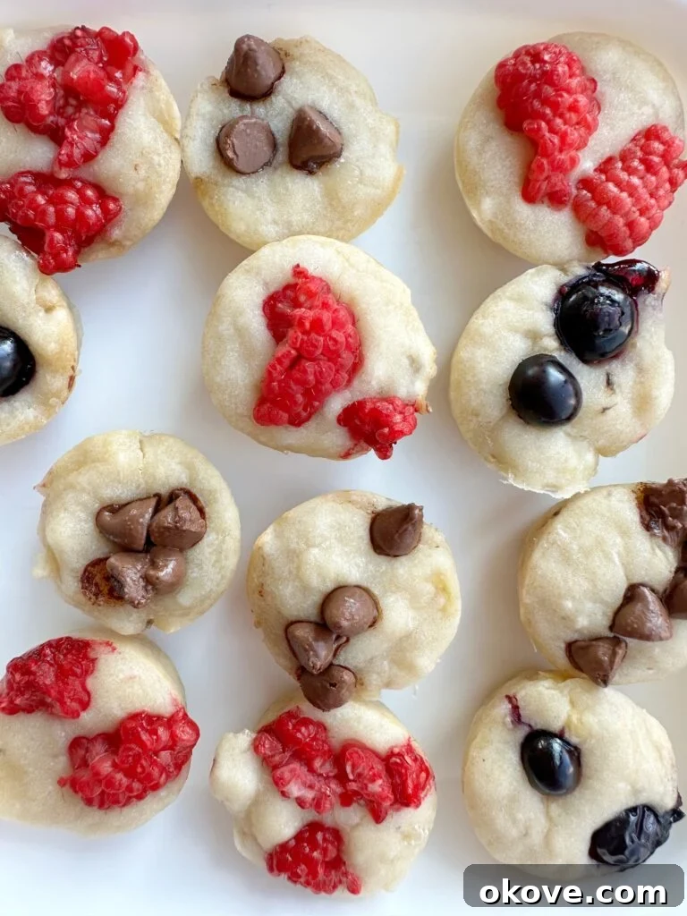 Grab-and-Go Pancake Bites 3 A white plate with several baked pancake bites that are topped with either raspberries blueberries or chocolate chips