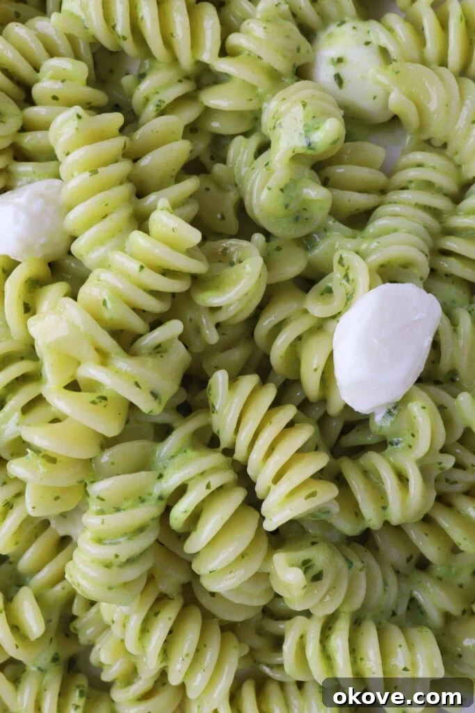 Garden Fresh Pesto Pasta 3 A close-up shot of creamy pesto pasta, highlighting the rich green sauce coating the pasta and the melting mozzarella balls, ready to be enjoyed.