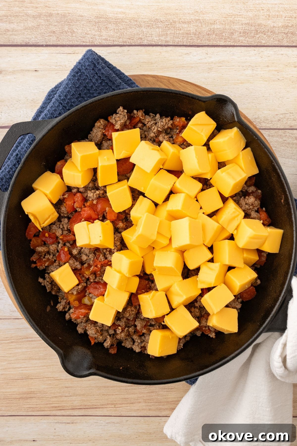 Rotel Fiesta Dip 5 Cubes of cheese being added to a skillet with cooked ground beef.