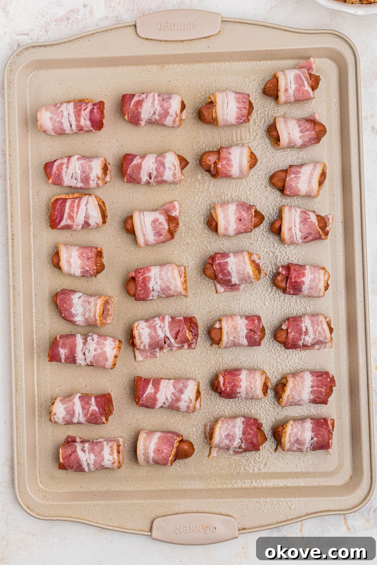 Bacon wrapped smokies on a baking sheet, before being coated in brown sugar and paprika and before being cooked. 