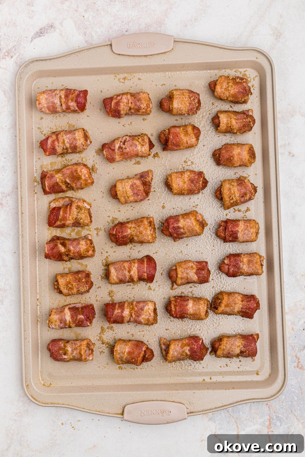 Bacon wrapped smokies, coated in brown sugar mixture, and placed evenly on a baking sheet. 