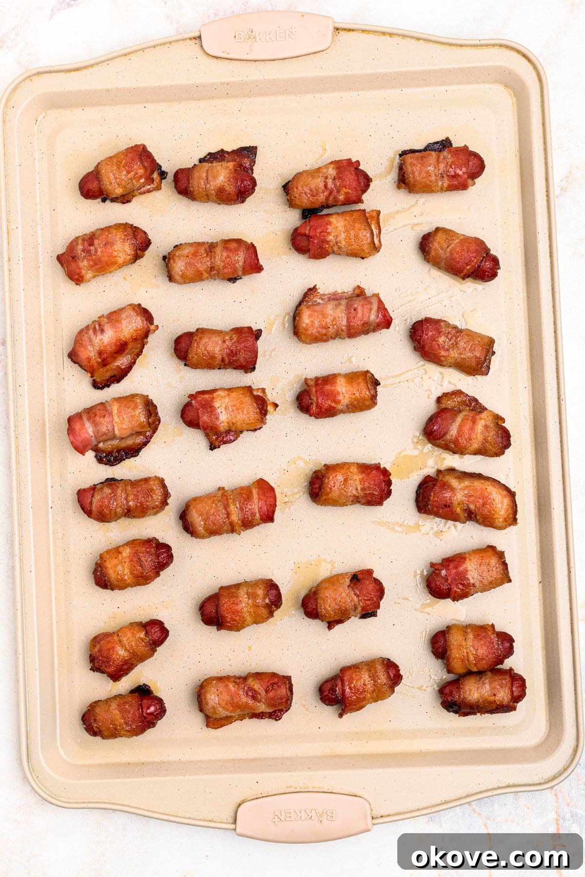 Golden crispy bacon wrapped smokies on a baking sheet.