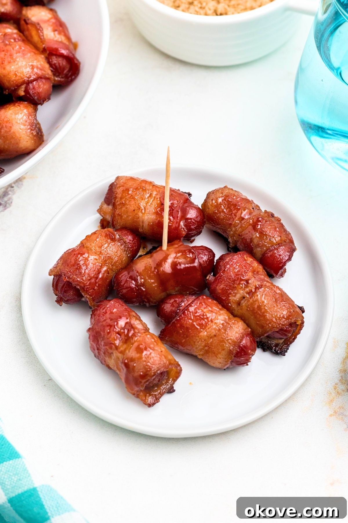 Bacon wrapped smokies on a small white plate with glasses of water on the table.
