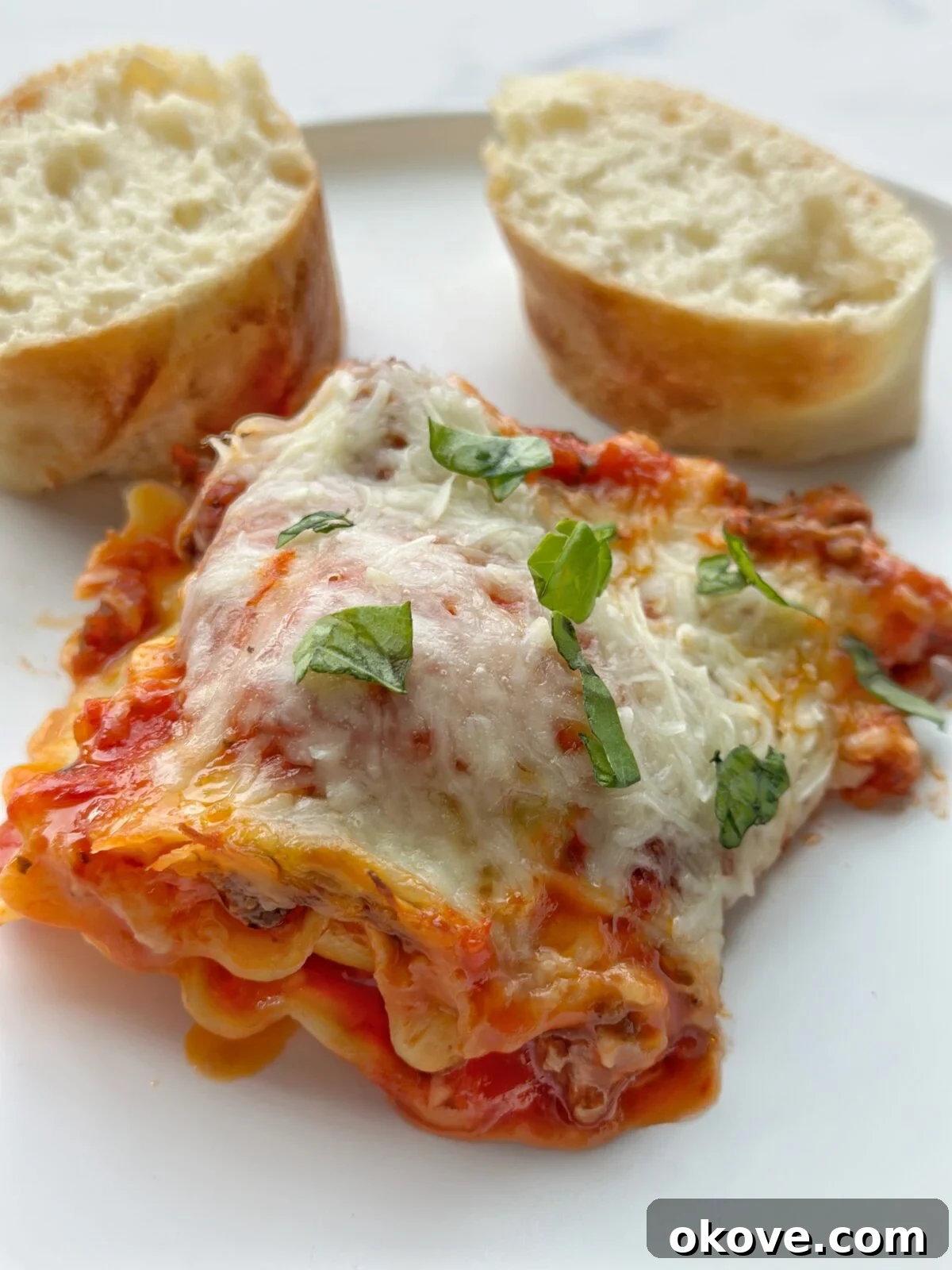 A generous serving of bubbly, cheesy ravioli lasagna alongside crisp sliced French bread, ready for a comforting family dinner.