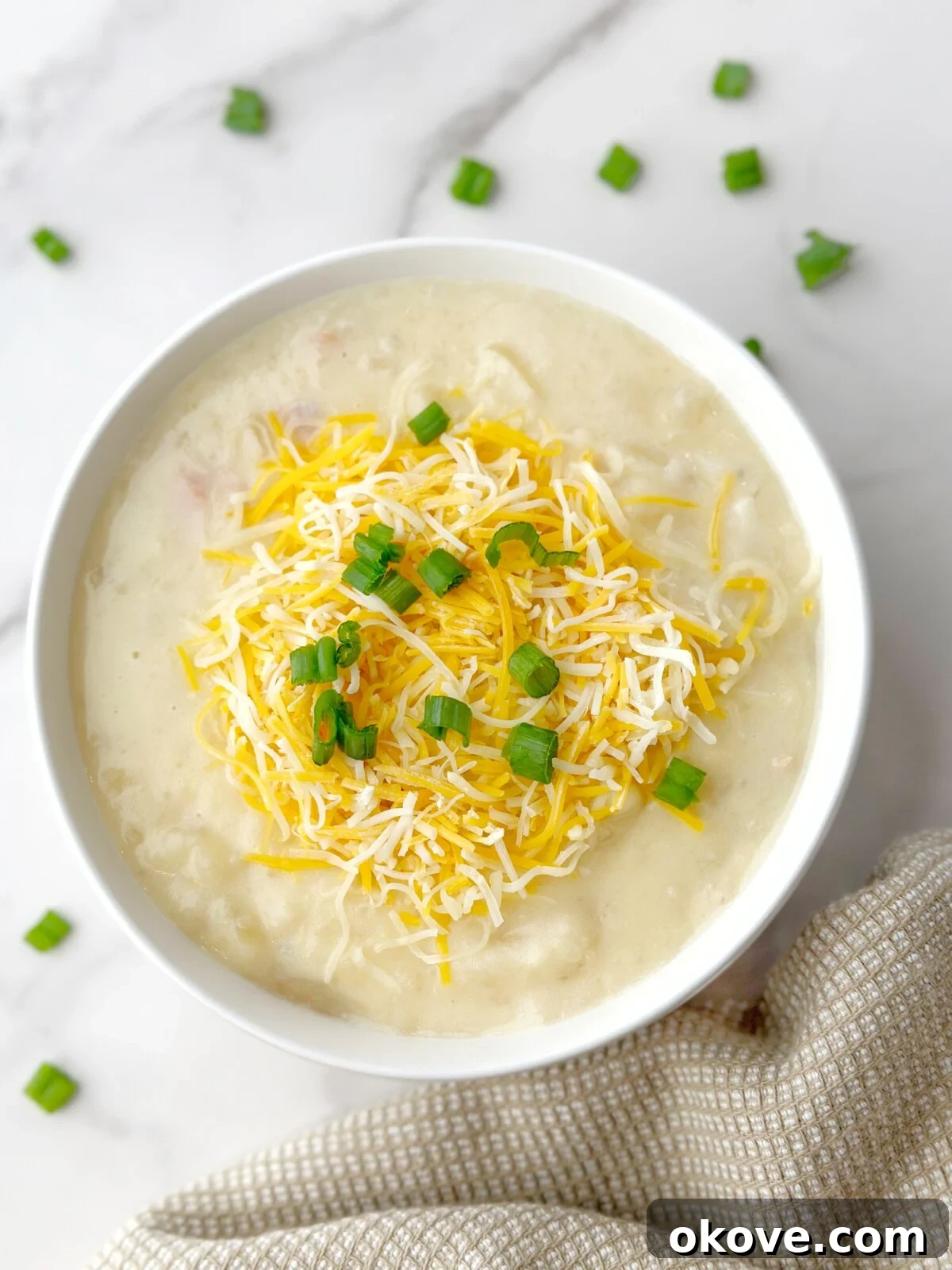 Rich and creamy loaded potato soup in a white bowl, generously topped with shredded cheddar cheese and fresh green onions, ready to be served on a cozy autumn evening.