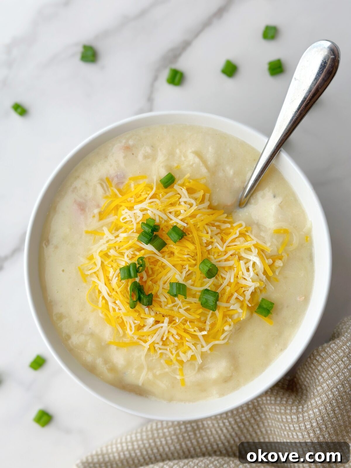 A steaming bowl of homemade loaded potato soup, adorned with melted cheddar cheese and freshly chopped green onions, promising warmth and comfort.