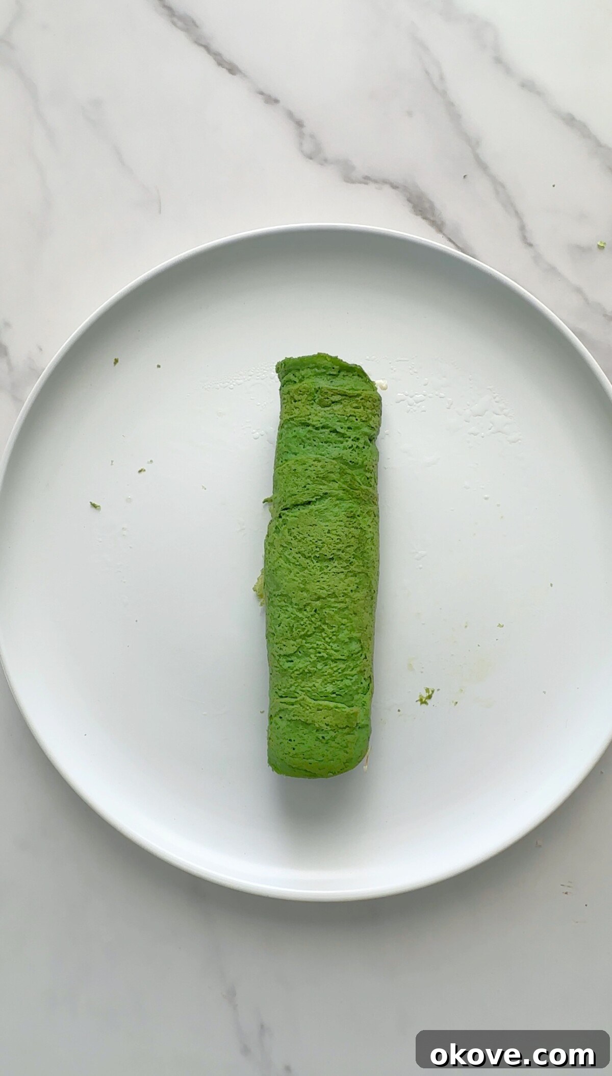An unsliced Hulk Roll Up, tightly rolled into a log shape, resting on a cutting board.