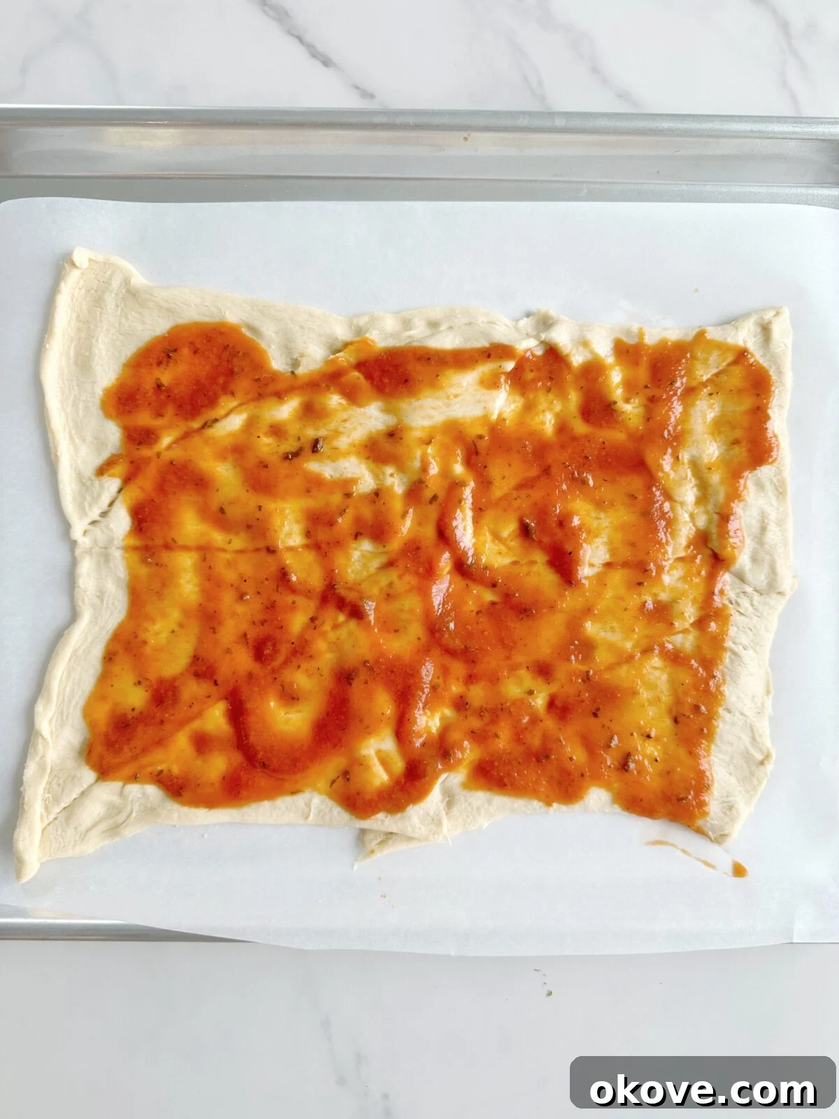 Savory Pizza Spirals 5 Flattened crescent roll dough covered with red pizza sauce and a generous layer of shredded mozzarella cheese, ready for toppings.