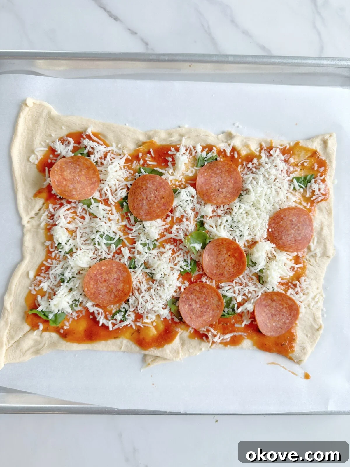 Savory Pizza Spirals 6 The uncooked pizza pinwheel dough fully topped with sauce, cheese, and pepperoni, rolled out flat before being cut.
