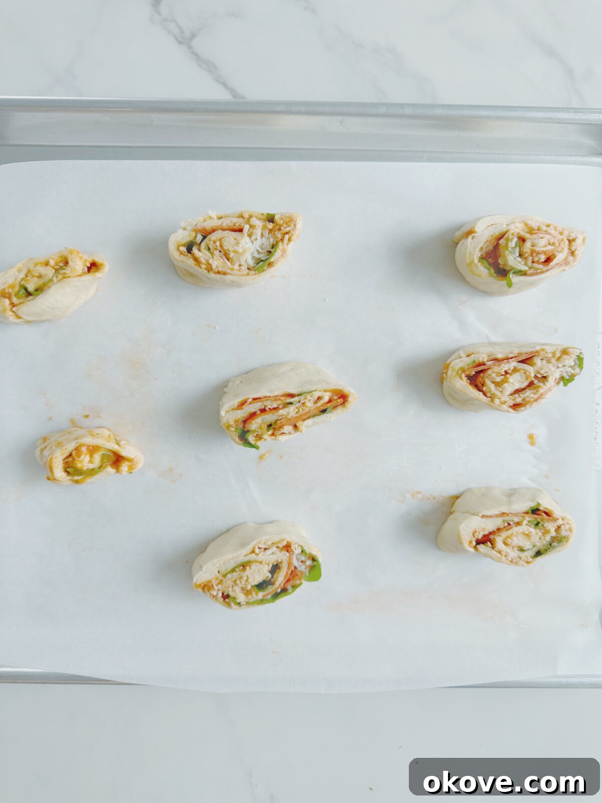 Savory Pizza Spirals 8 Freshly sliced, uncooked pizza pinwheels neatly arranged on a parchment-lined baking sheet, showing their spiral design before baking.