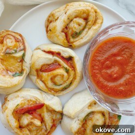 Pizza pinwheels on a plate with a side of marinara sauce
