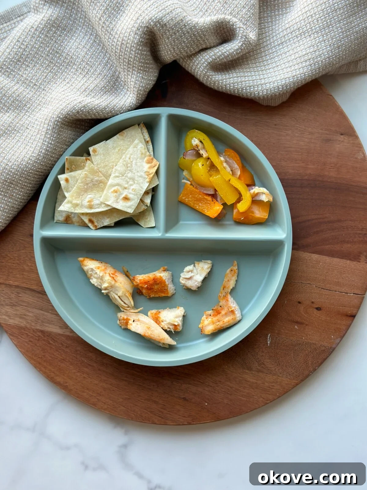 Deconstructed sheet pan fajita ingredients on a divided plate, perfect for toddler self-feeding, showing chicken, bell peppers, and onion separately.