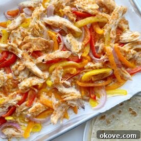 Sheet pan fajitas with chicken and colorful vegetables served alongside tortillas and toppings.