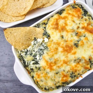 Creamy Spinach Artichoke Delight 9 Creamy spinach artichoke dip in a square baking dish, with a tortilla chip scooping out a generous portion.