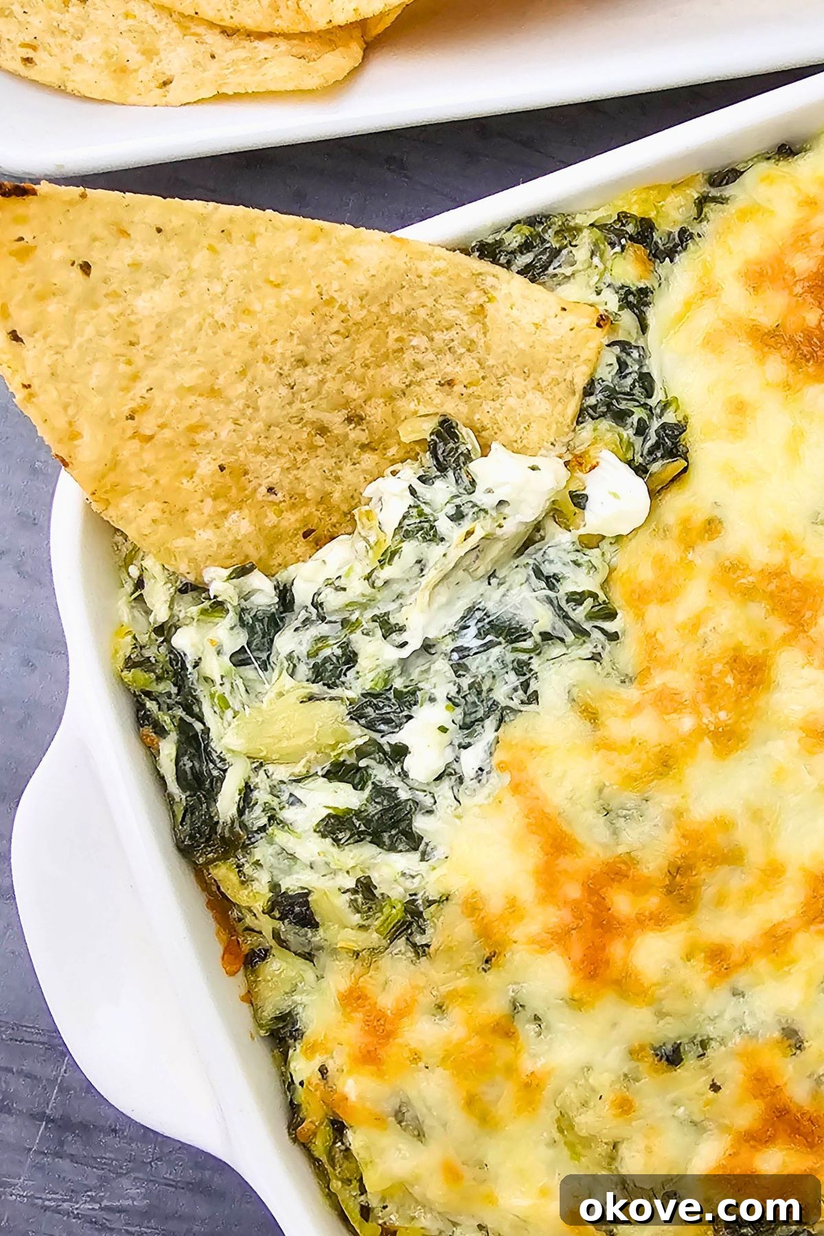 Creamy Spinach Artichoke Delight 8 Close-up of creamy spinach artichoke dip in a square dish, with a single tortilla chip perfectly loaded with dip.