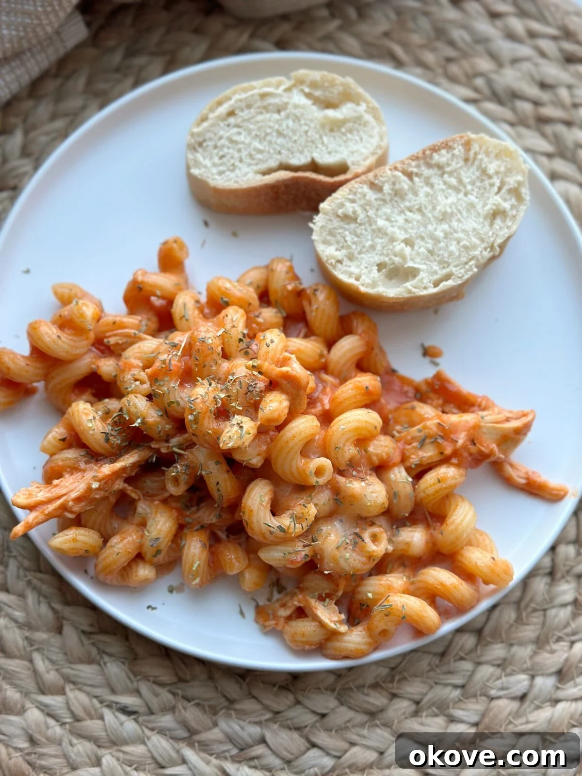 Silky Chicken Pasta Delight 2 Creamy chicken pasta on a plate with a side of sliced bread, ready to be enjoyed by the family.