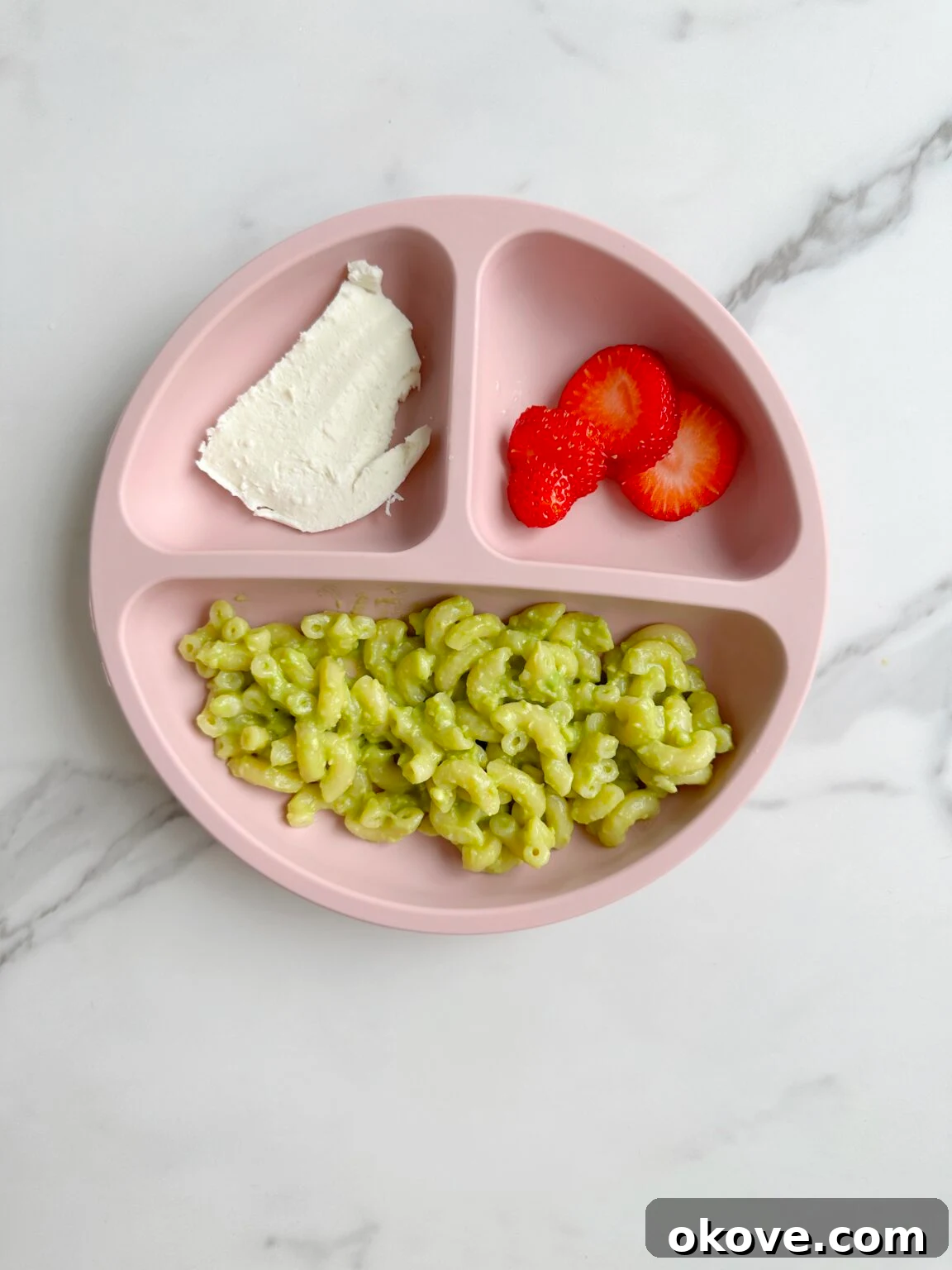 Avocado pasta in a divided plate with sliced strawberry and mozzarella cheese