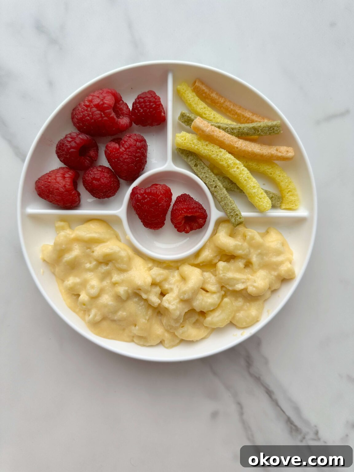 A divided plate with cauliflower mac n cheese, veggie straws, and raspberries