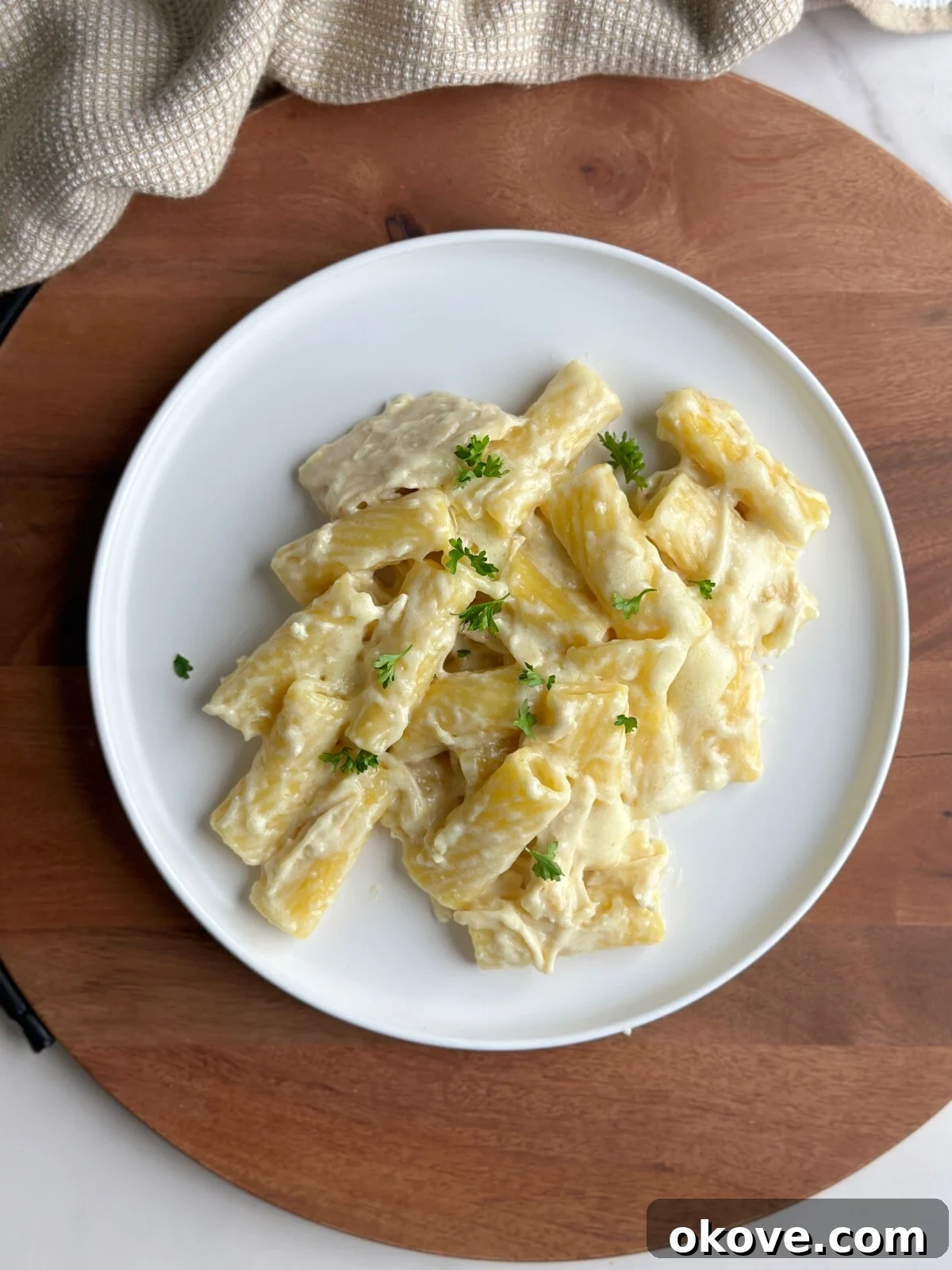 Effortless Creamy Chicken Alfredo 2 Creamy Slow Cooker Chicken Alfredo on a white plate, garnished with fresh parsley.