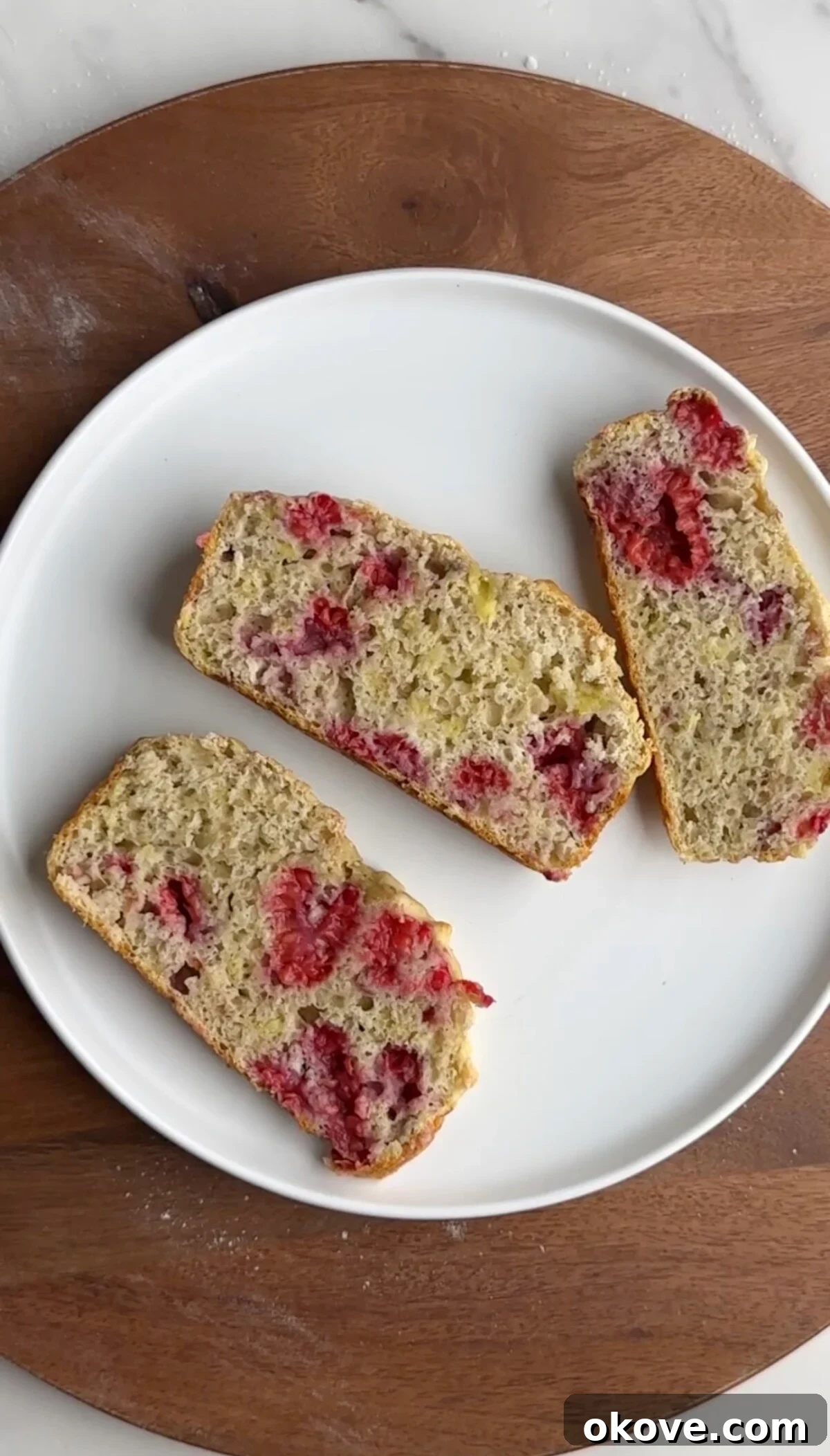 Luscious Raspberry Banana Loaf 2 Slices of fluffy raspberry banana bread on a pristine white plate, garnished with fresh raspberries.