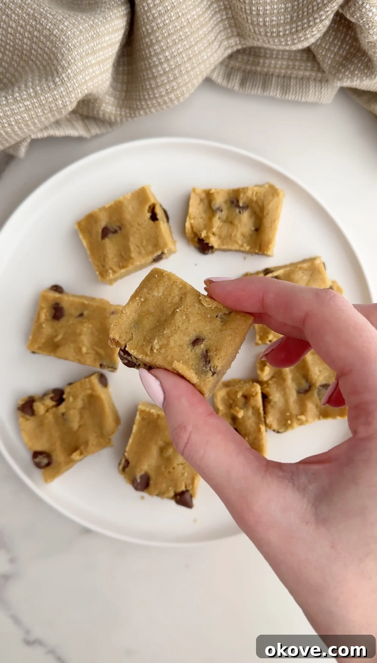 A hand holding a healthy cookie dough bar, showcasing its delicious, chewy texture and chocolate chips.