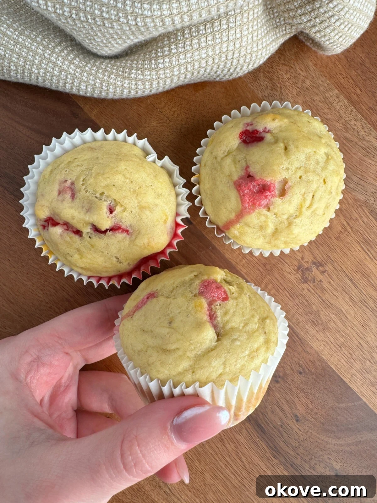 Irresistible Raspberry Muffins 2 Three golden-brown banana raspberry muffins with visible raspberries on a rustic wooden background.