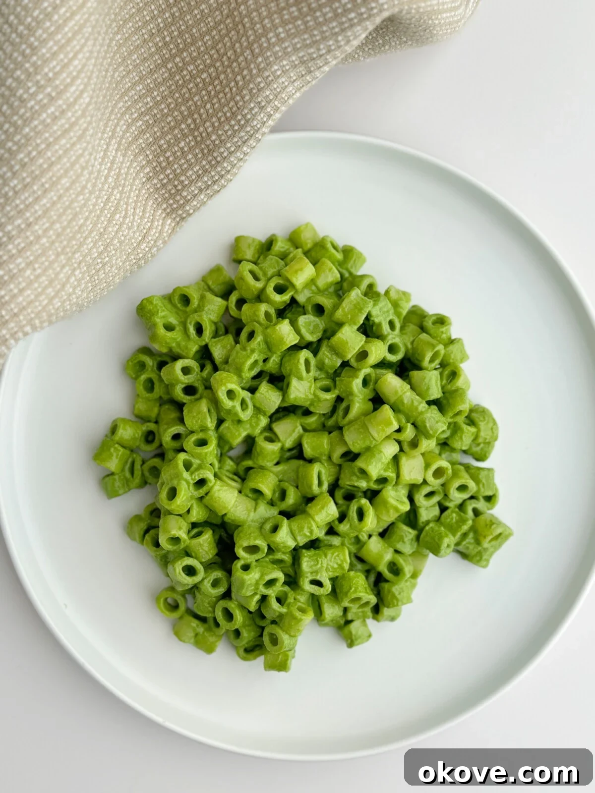 Velvet Spinach Pasta 2 A close-up shot of creamy spinach pasta with a vibrant green sauce on a white plate, ready to be served to a family or toddler.