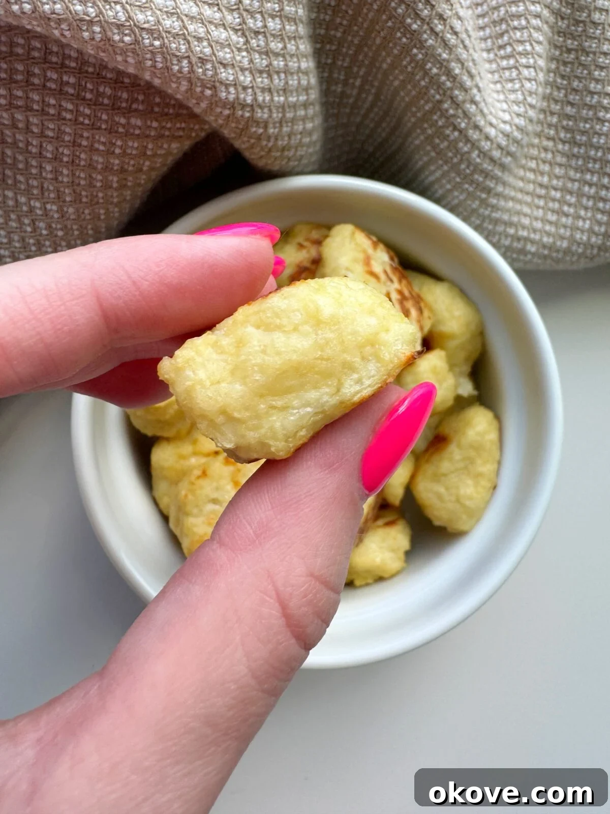 A child's hand happily holding a golden, baked cauliflower nugget, ready to take a bite.