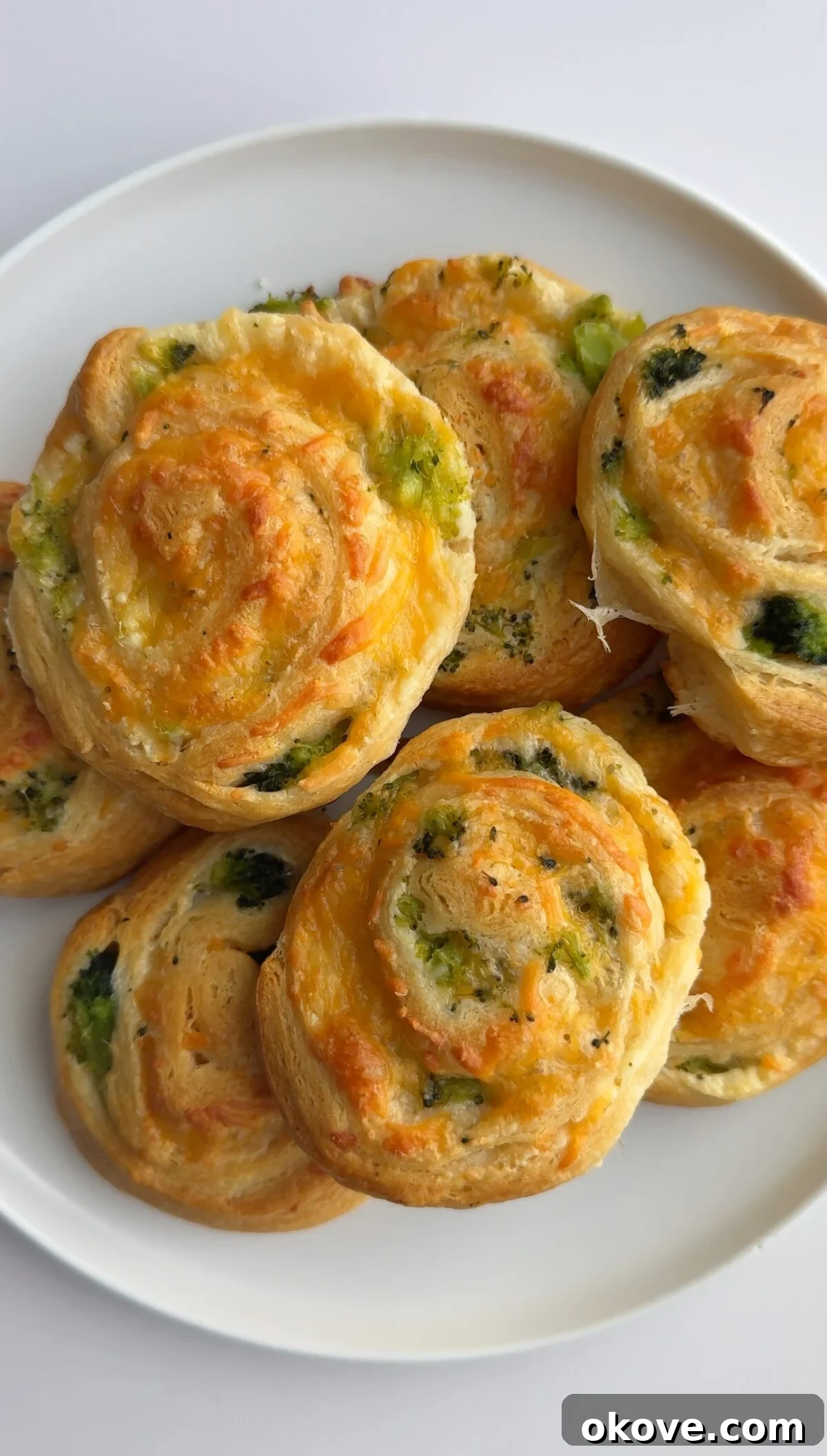 Broccoli Cheddar Swirls 2 Many golden-brown broccoli cheese pinwheels for toddlers on a white plate